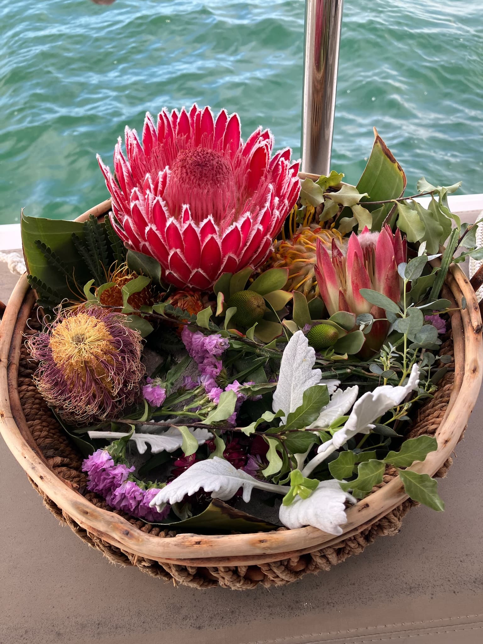A woven basket of protea and native blooms resting on deck above the water.